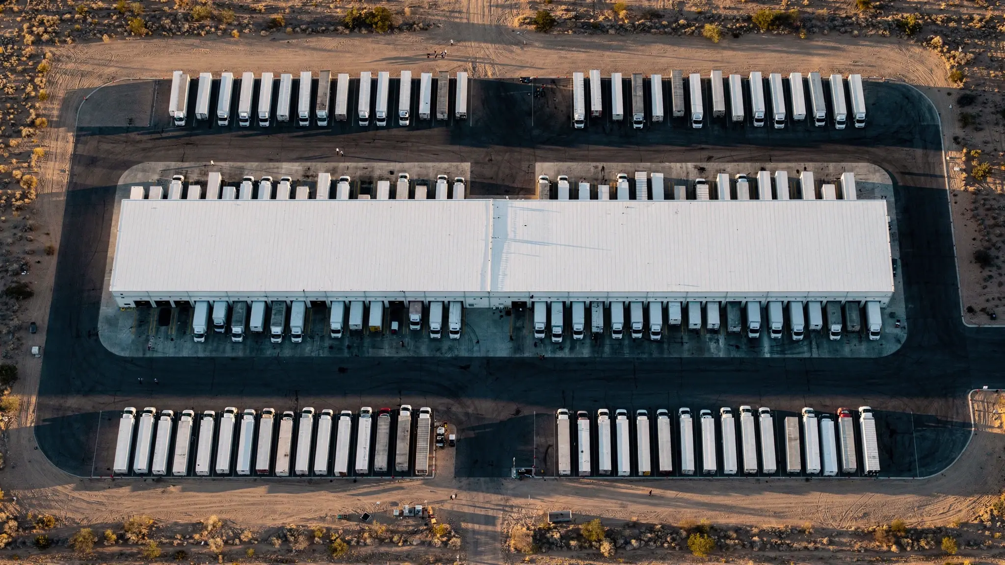 Vista aérea de un almacén de cross-dock con tractocamiones estacionados en los andenes de ambos lados, con luz de la hora dorada.